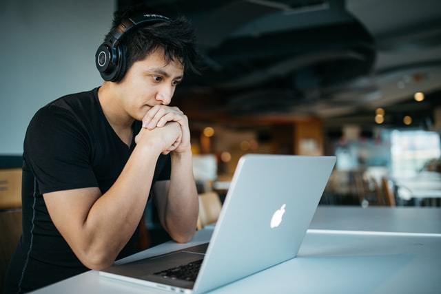 A young man wearing headphones staring intently at his laptop screen