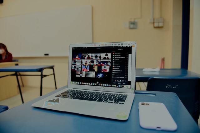 A laptop standing on a desk in what appears to be a classroom and has a meeting software running with multiple people in the session and their cameras on.