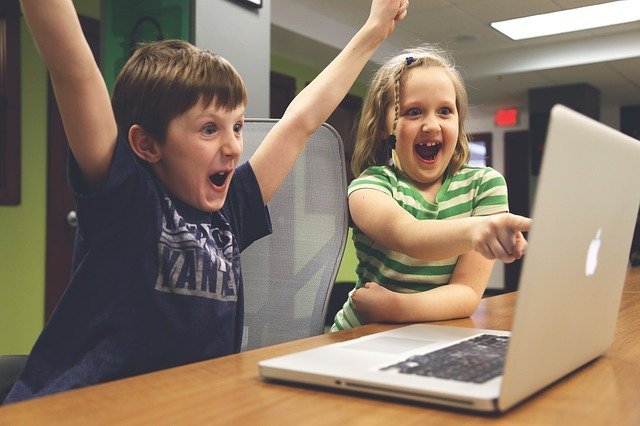 Children at a laptop computer. The boy has his arms raised in the air and the girl points at something excitedly on the computer screen