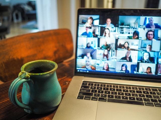 A photo of a laptop screen of a person in a meeting with others whose video is on and showing their face and a coffee cup next to the laptop